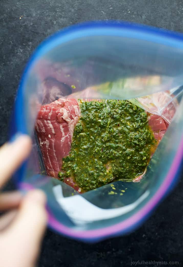 steak being marinaded with green sauce in a plastic bag