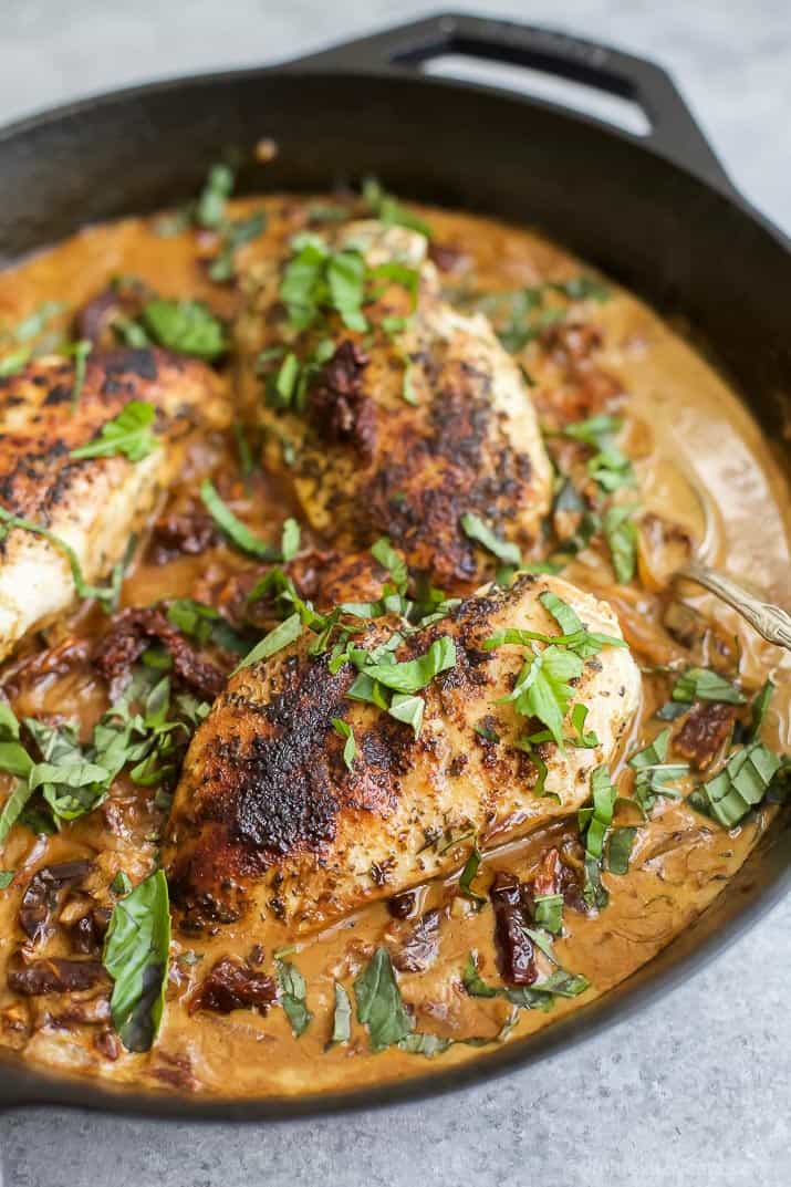 Creamy sun dried tomato chicken in a skillet topped with fresh herbs
