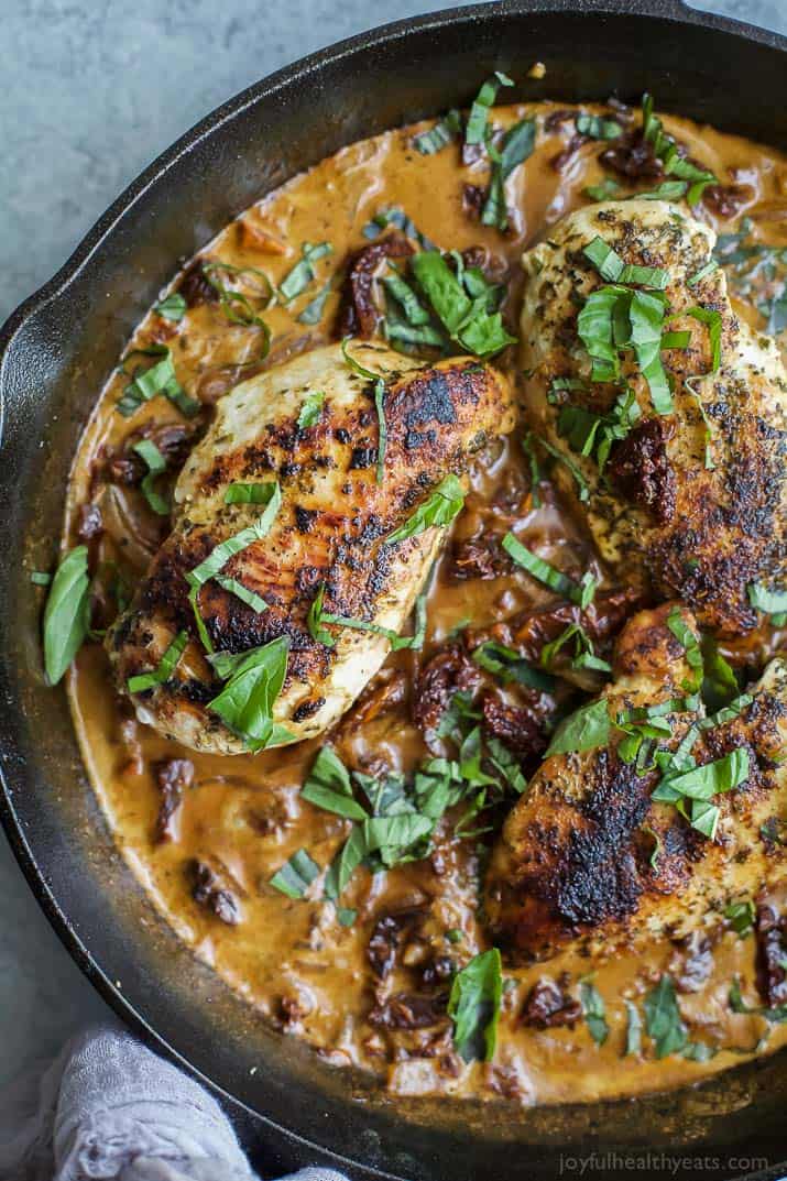 Chicken breasts in creamy sundried tomato sauce in a skillet topped with fresh herbs