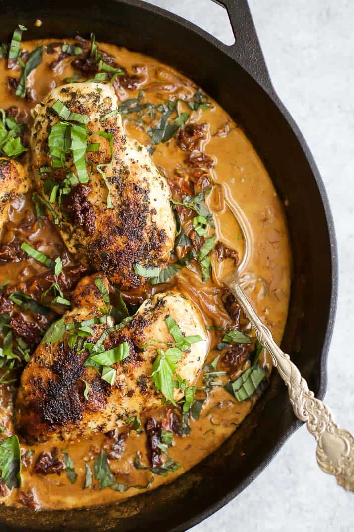 Top view of sun dried tomato chicken in a skillet with fresh herbs