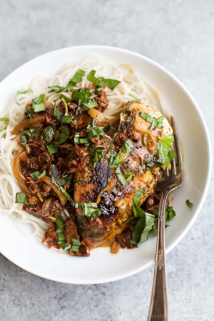 Top view of sun dried tomato chicken with fresh herbs over pasta in a bowl