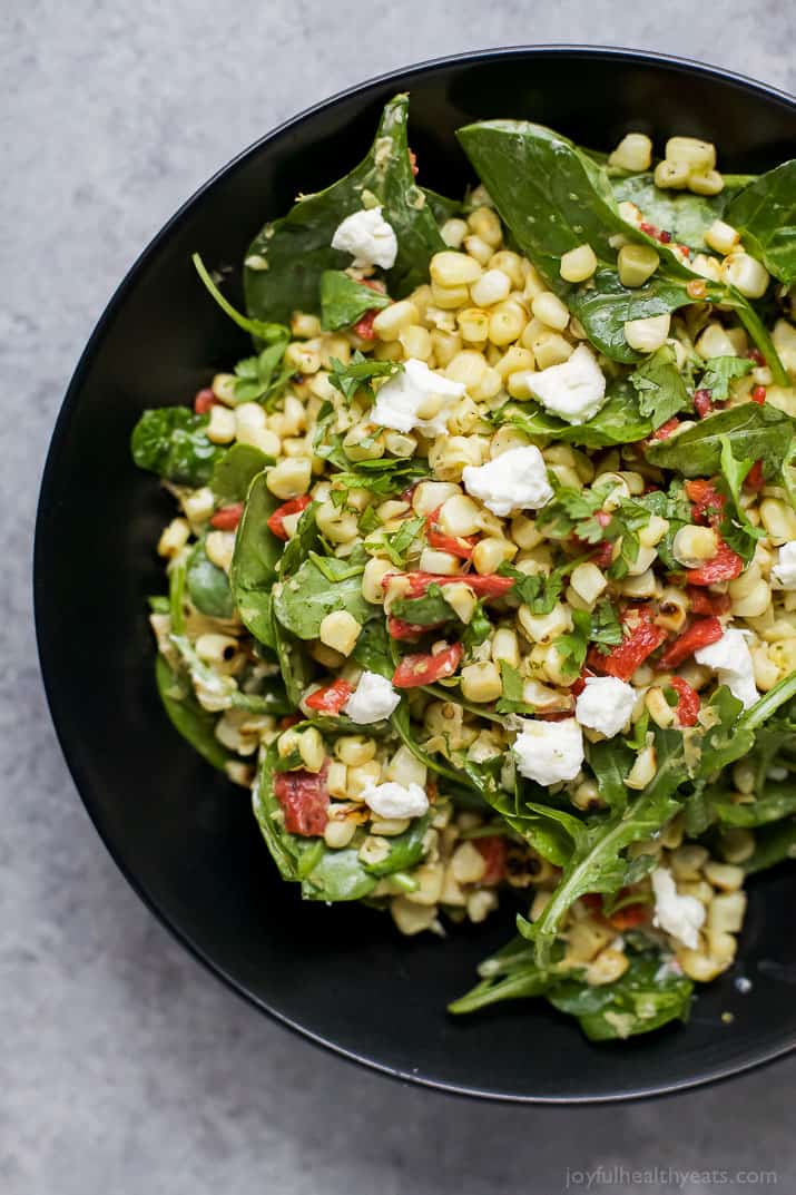 Top view of GRILLED CORN SALAD with fresh greens, roasted red pepper, and goat cheese