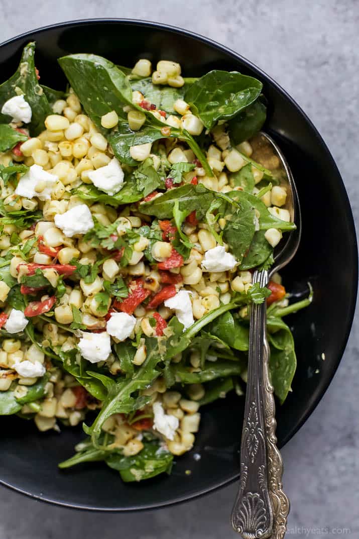 Top view of GRILLED CORN SALAD with fresh greens, roasted red pepper, and goat cheese in a bowl