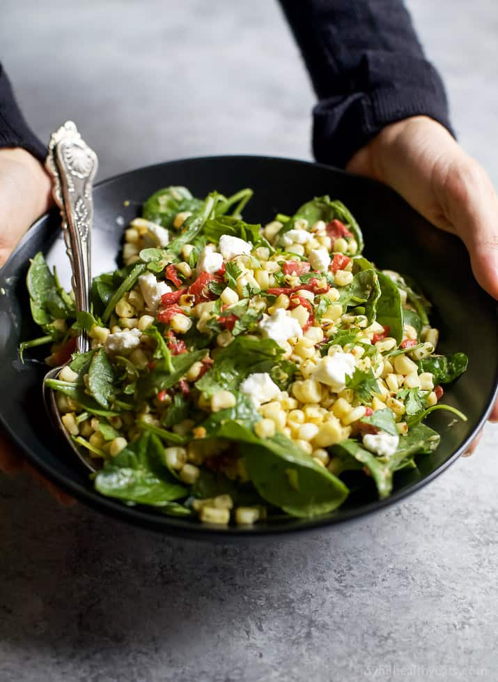 Top view of GRILLED CORN SALAD with fresh greens, roasted red pepper, and goat cheese in a bowl