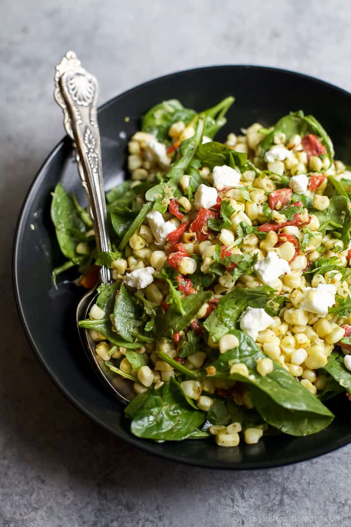 Top view of GRILLED CORN SALAD with fresh greens, roasted red pepper, and goat cheese in a bowl