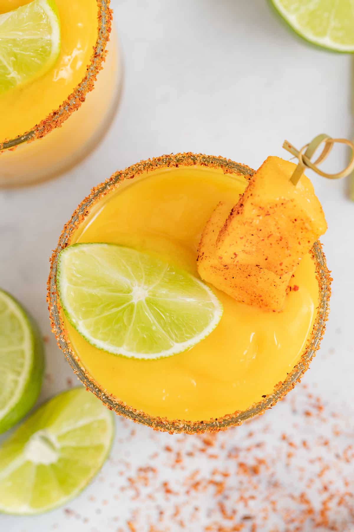 Served in chili-rimmed glasses, this frozen mango margarita is the boozy, tropical drink you need to beat the heat this summer. Overhead of frozen mango margarita.