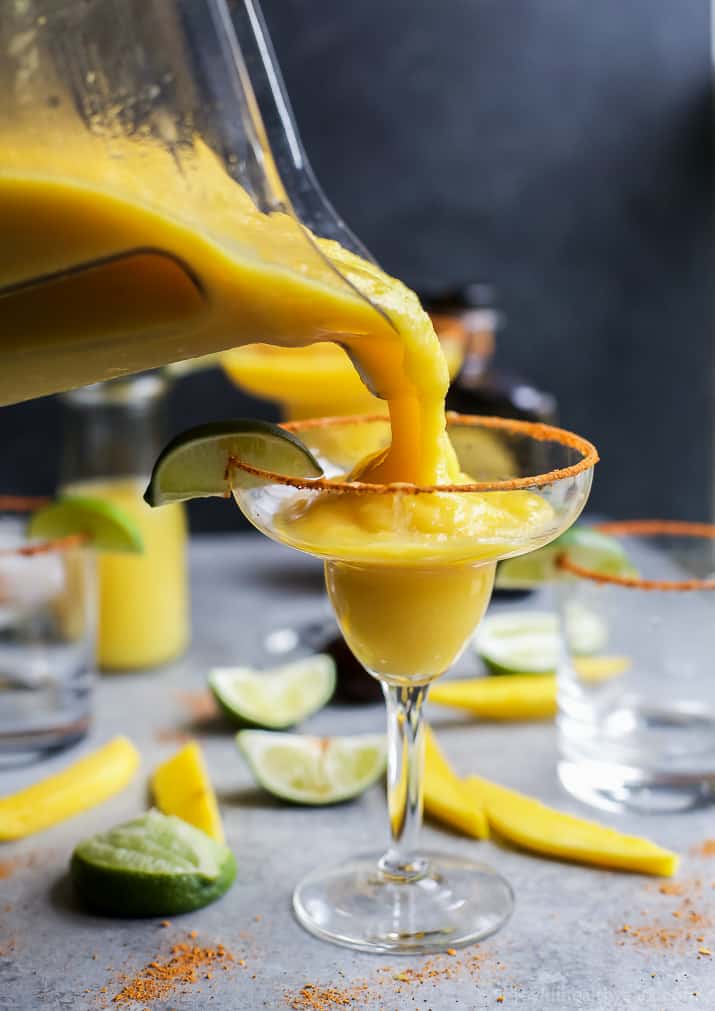 Frozen Mango Margarita being poured into a glass with a chili lime salt rim