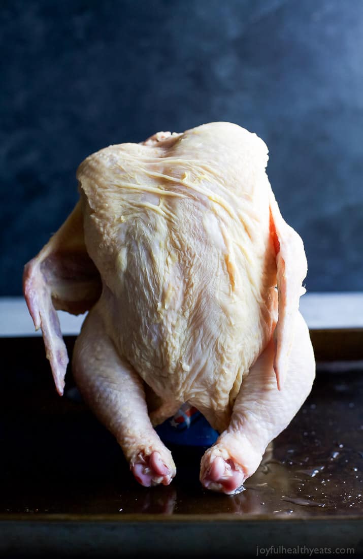Whole raw chicken standing upright on a pan