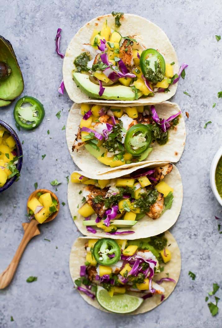 Vue de dessus de quatre TACOS DE POISSON GRILLÉS garnis de SALSA de MANGUE fraîche, d'avocat et de Chimichurri