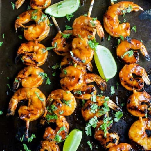 Four honey sriracha grilled shrimp skewers on a serving platter with a silicone basting brush