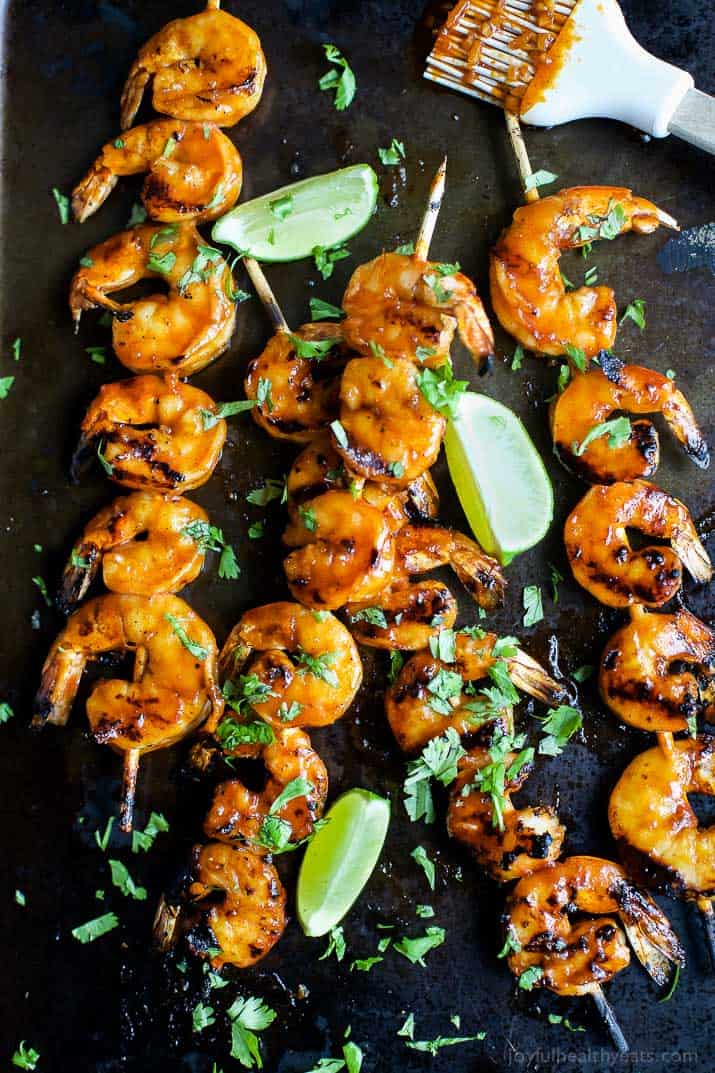 Four honey sriracha grilled shrimp skewers on a serving platter with a silicone basting brush