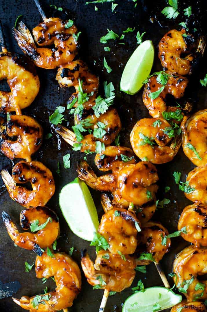 Four sweet and spicy shrimp skewers laid down on top of a black surface