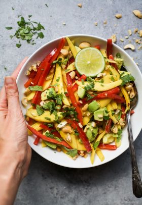 thai mango avocado salad in a bowl with hands holding the bowl