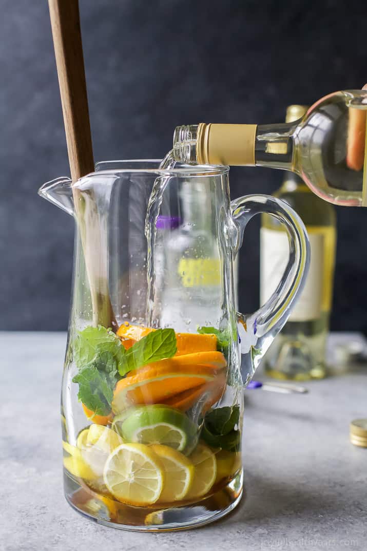 White wine being poured over citrus fruit and fresh mint in a pitcher