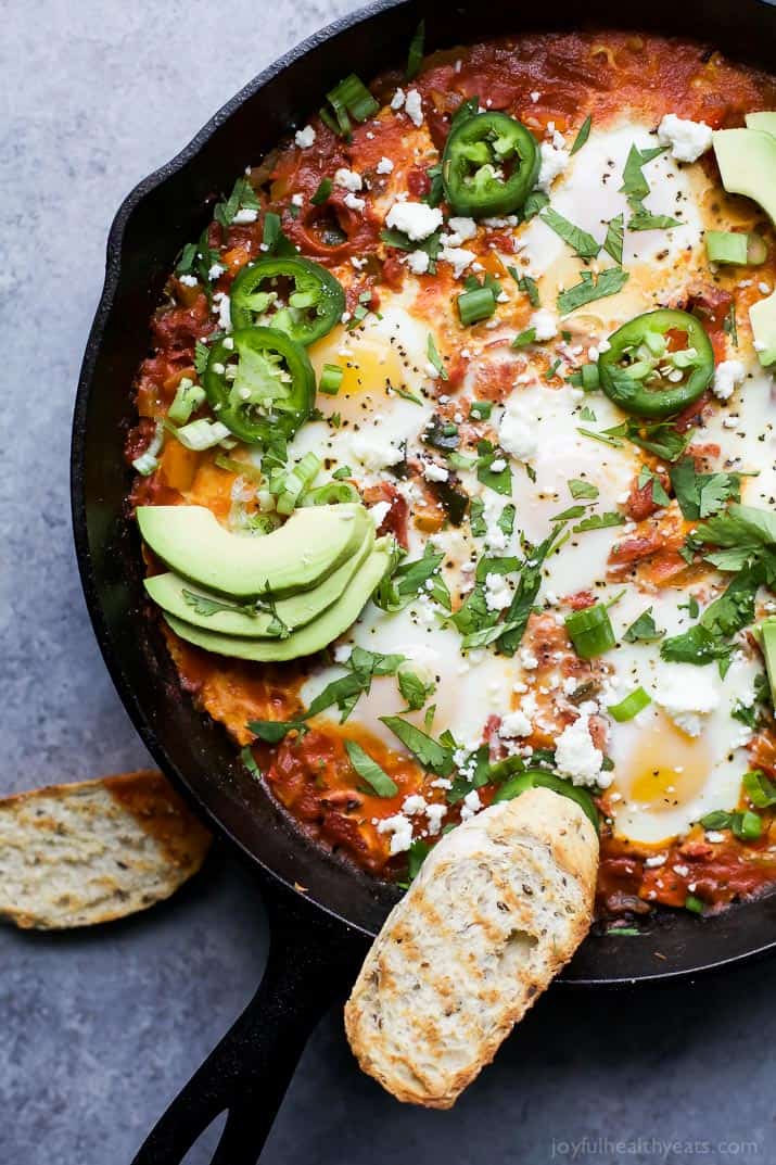 A skillet full of shakshouka topped with sliced jalapeño and avocado