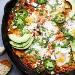 A pan of shakshuka on a countertop beside a slice of bread that's been dipped into the sauce