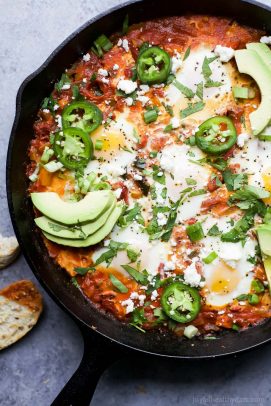 A pan of shakshuka on a countertop beside a slice of bread that's been dipped into the sauce