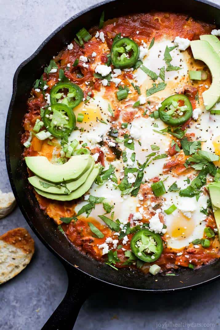 A pan of shakshuka on a countertop beside a slice of bread that's been dipped into the sauce