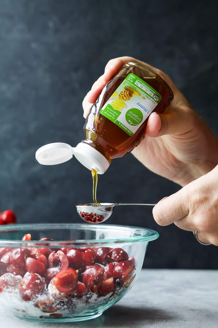 Honey being measured into a mixing bowl with halved cherries