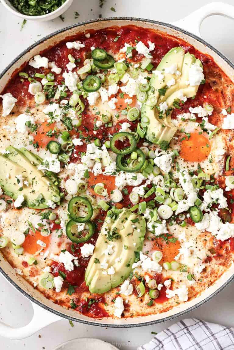 Freshly-made one-skillet shakshuka with queso fresco, cilantro, green onions, jalapeños, and creamy avocado on top.