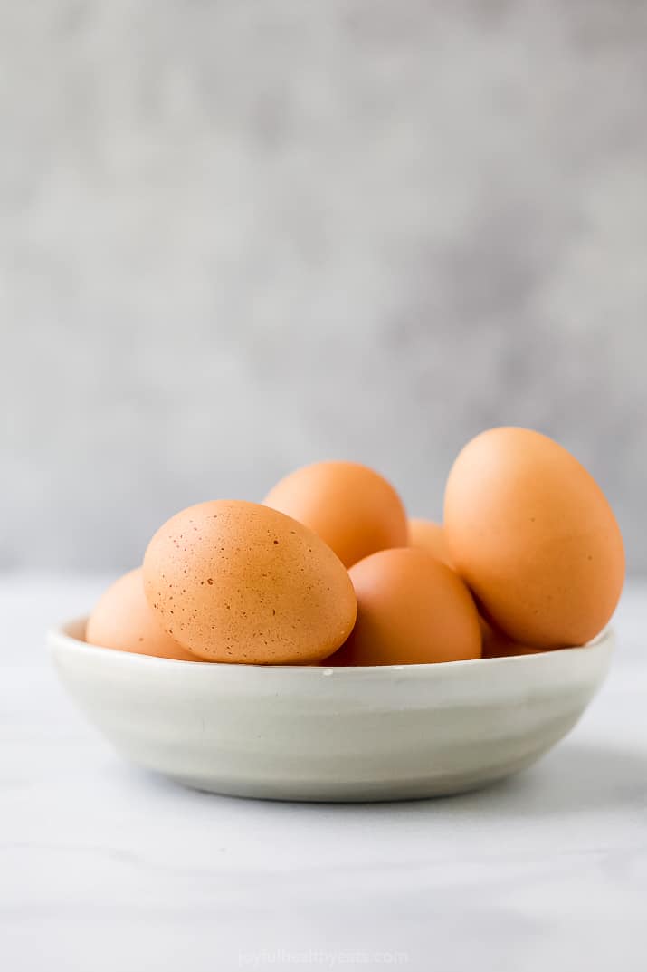 Side view of a bowl of raw brown eggs in a shallow bowl