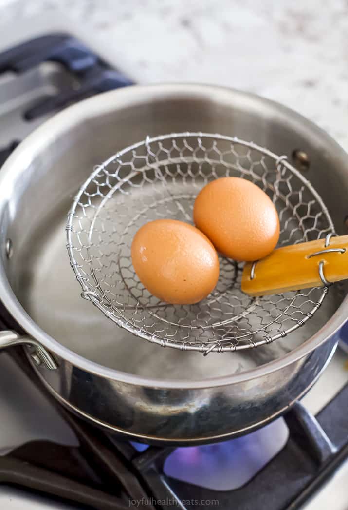 Two brown eggs on a skimmer spoon over a pot of boiling water