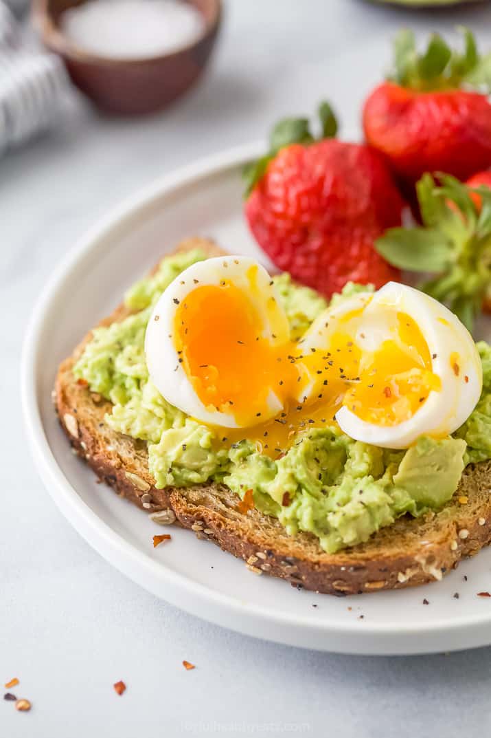 Close-up of smashed avocado toast topped with a soft-boiled egg served with fresh strawberries on a plate