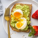Close-up overhead view of smashed avocado toast topped with a soft-boiled egg served with fresh strawberries