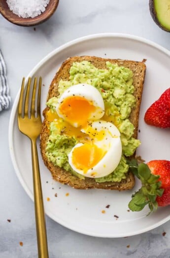 Close-up overhead view of smashed avocado toast topped with a soft-boiled egg served with fresh strawberries