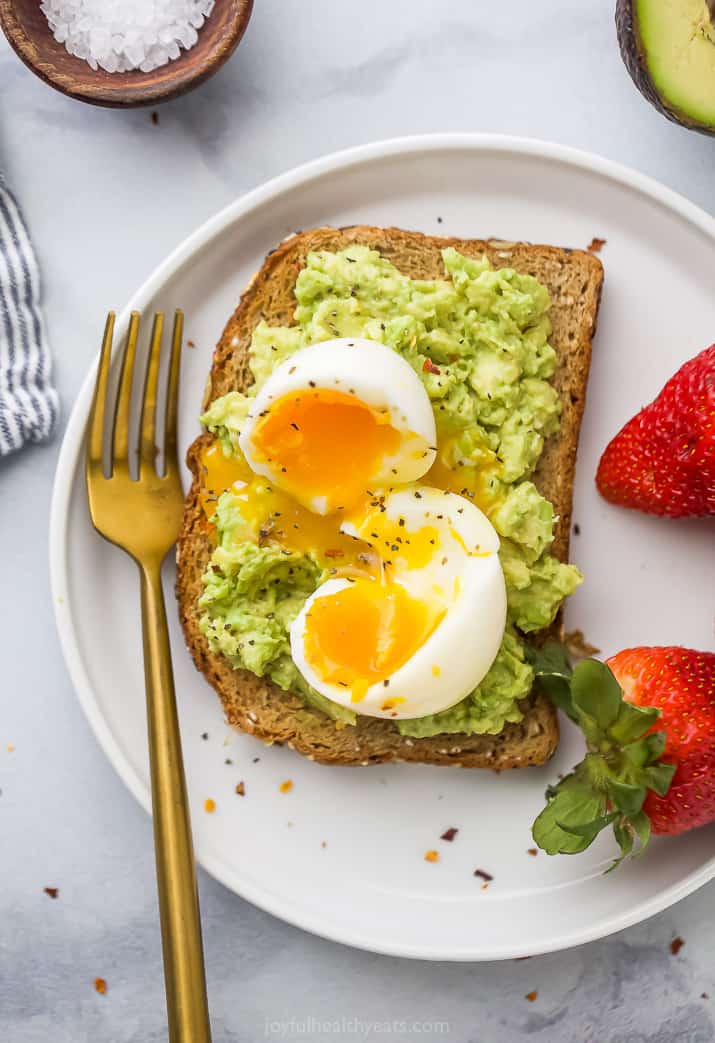 Close-up overhead view of smashed avocado toast topped with a soft-boiled egg served with fresh strawberries