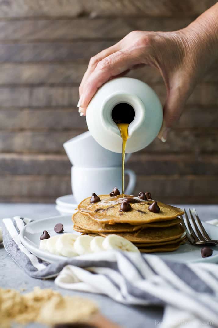 Maple syrup being poured over a stack of Flourless Peanut Chocolate Chip Pancakes