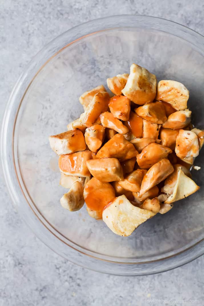 Top view of chicken pieces with buffalo sauce in a mixing bowl