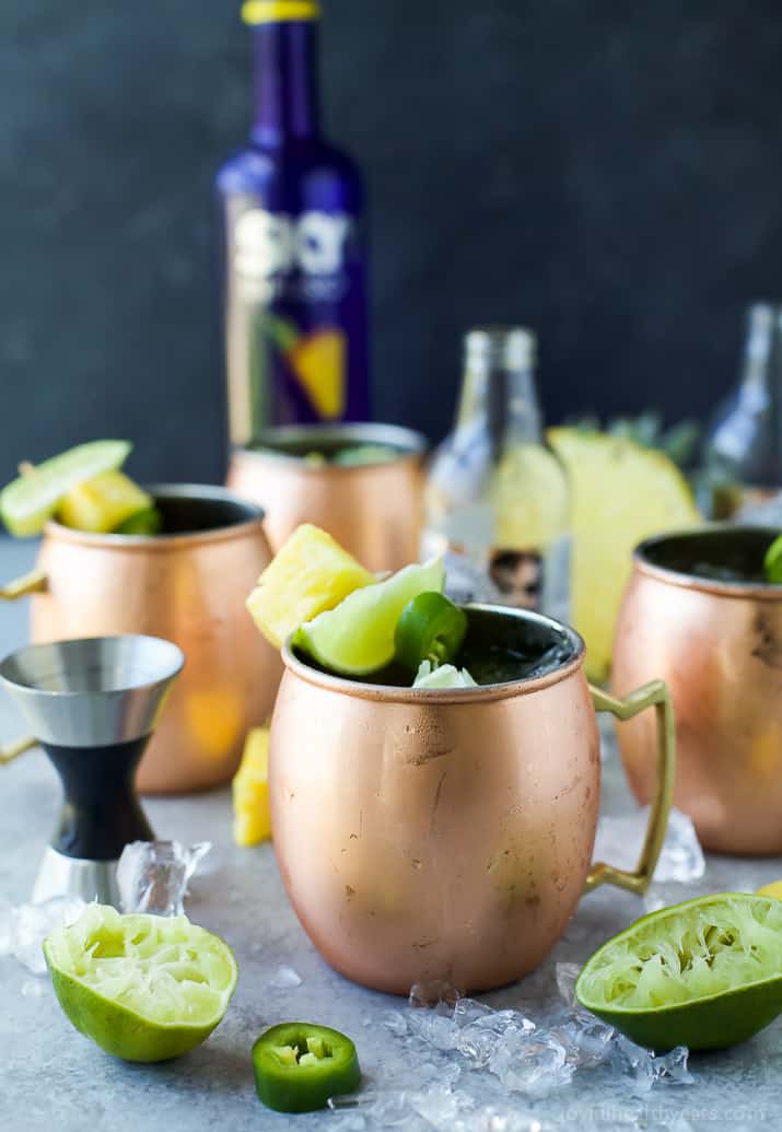 A couple of Moscow Mules on a table in copper cups surrounded by ingredients 