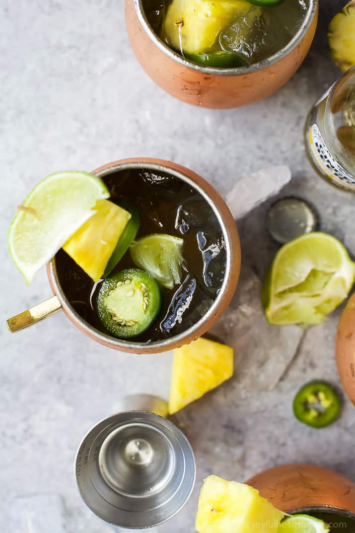 Top view of a Jalapeno Pineapple Moscow Mule with limes, pineapple and jalapenos on a table