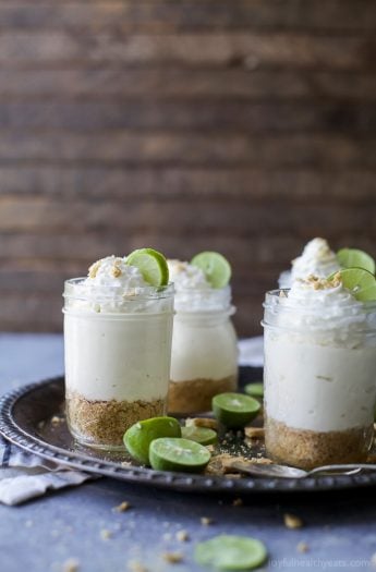 A few jars of Easy No-Bake Key Lime Cheesecake topped with whipped cream and lime wedges.