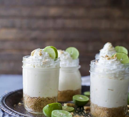 A few jars of Easy No-Bake Key Lime Cheesecake topped with whipped cream and lime wedges.