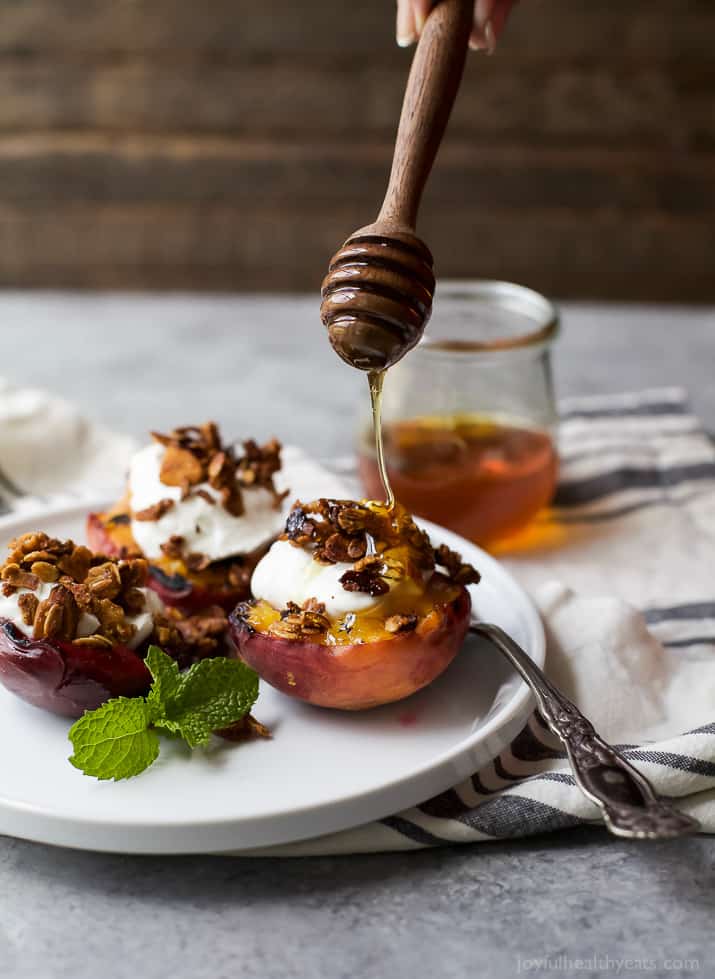 Honey being drizzled over Grilled Stone Fruit halves topped with Vanilla Yogurt & Homemade Granola on a plate