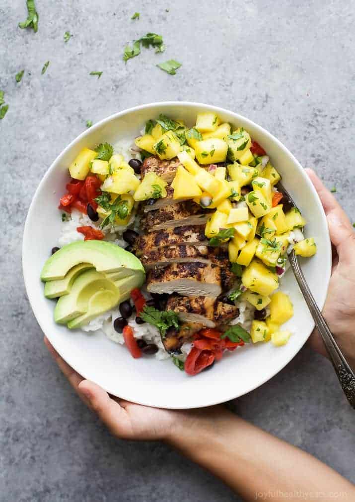 Hands holding a bowl with jerk chicken and pineapple salsa