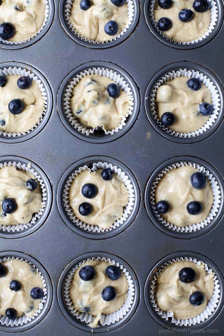 A muffin tin fitted with liners that are filled with blueberry muffin batter