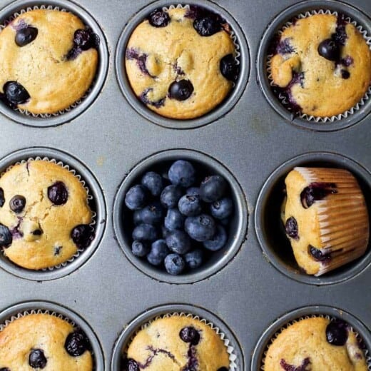 An overhead shot of a pan full of baked muffins with fresh berries scattered about