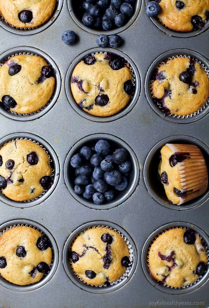 Studded with fresh berries and spiced with warm cinnamon, these Healthy Blueberry Muffins are a quick & easy make-ahead breakfast or snack! An overhead shot of a pan full of baked muffins with fresh berries scattered about