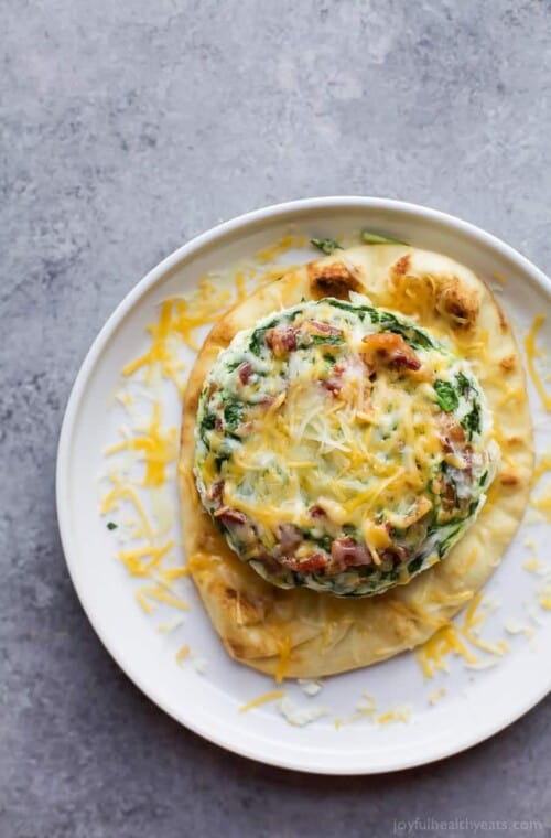 A plate of Bacon Egg White Breakfast Pizza topped with cheese and spinach.