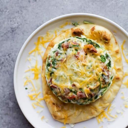 A plate of Bacon Egg White Breakfast Pizza topped with cheese and spinach.