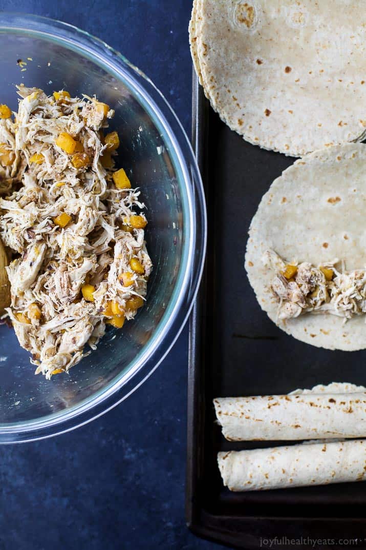 A bowl of shredded chicken and butternut squash filling next to tortillas for taquitos