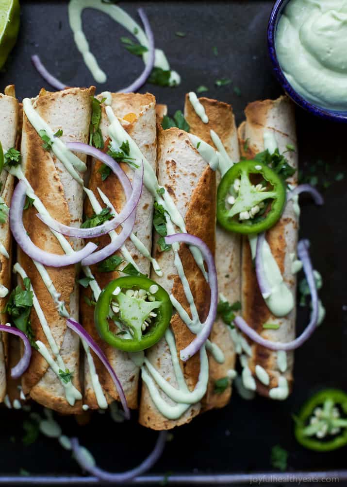 Cheesy Butternut Squash Chicken Taquitos drizzled with an Avocado Crema and garnished with sliced jalapenos and red onion