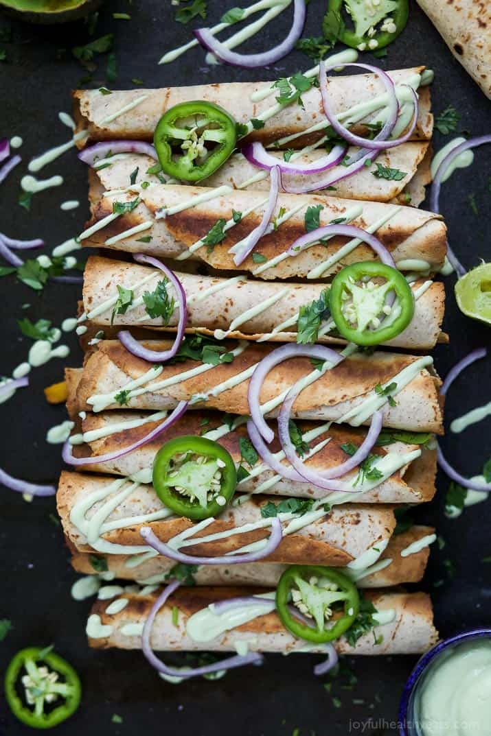 Cheesy Butternut Squash Chicken Taquitos drizzled with an Avocado Crema garnished with sliced jalapenos and red onion
