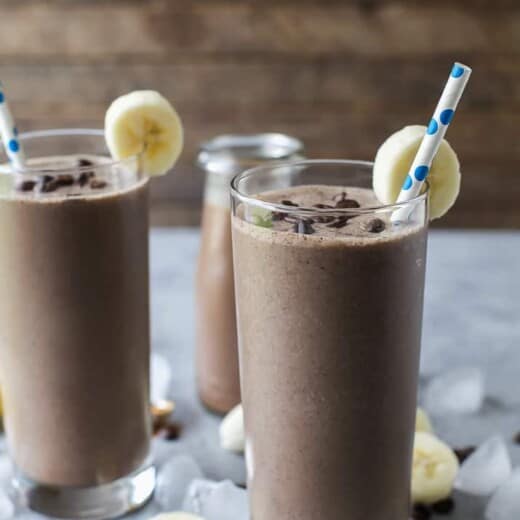 Two glasses full of Cafe Mocha Smoothie served with banana wedges and a straw