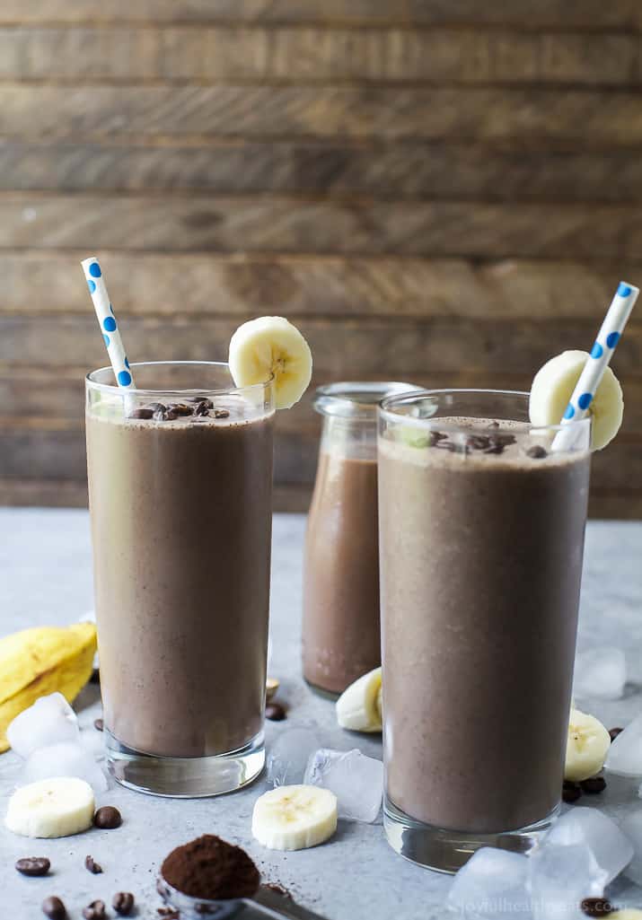 Two tall glasses of Cafe Mocha Smoothie garnished with a banana slice and topped with coffee beans and a straw