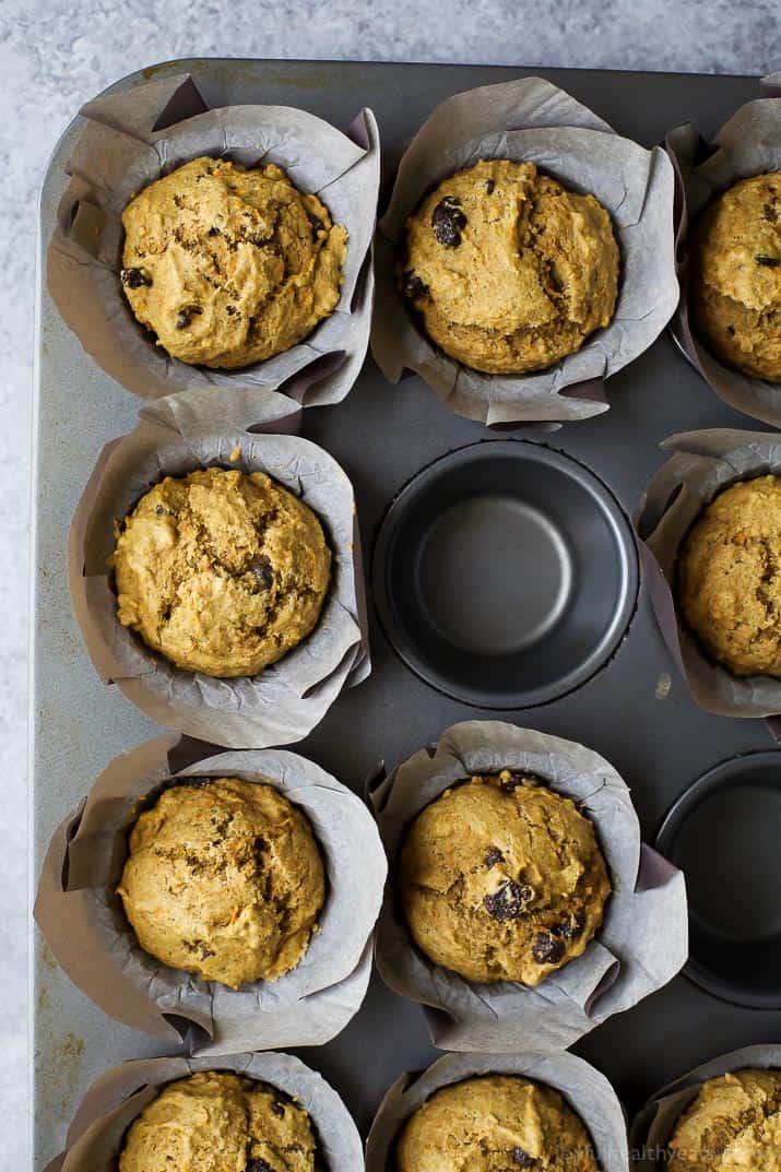 Top view of a tin of Healthy Carrot Cake Muffins in parchment liners with a couple muffins removed