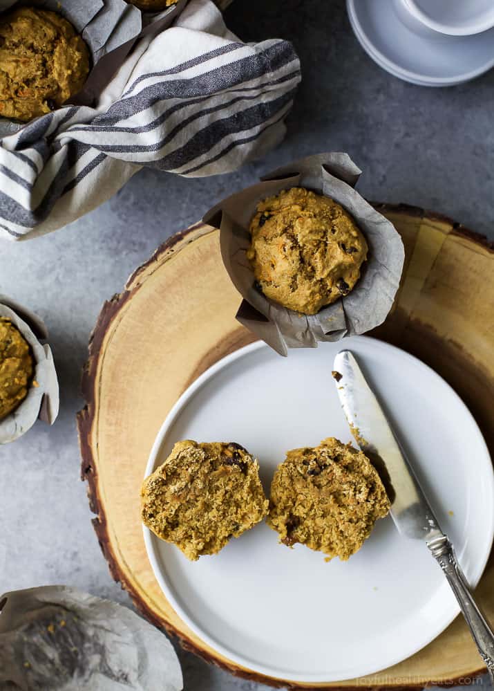 Top view of a halved Healthy Carrot Cake Muffin on a plate next to another Carrot Cake Muffin in a parchment wrapper